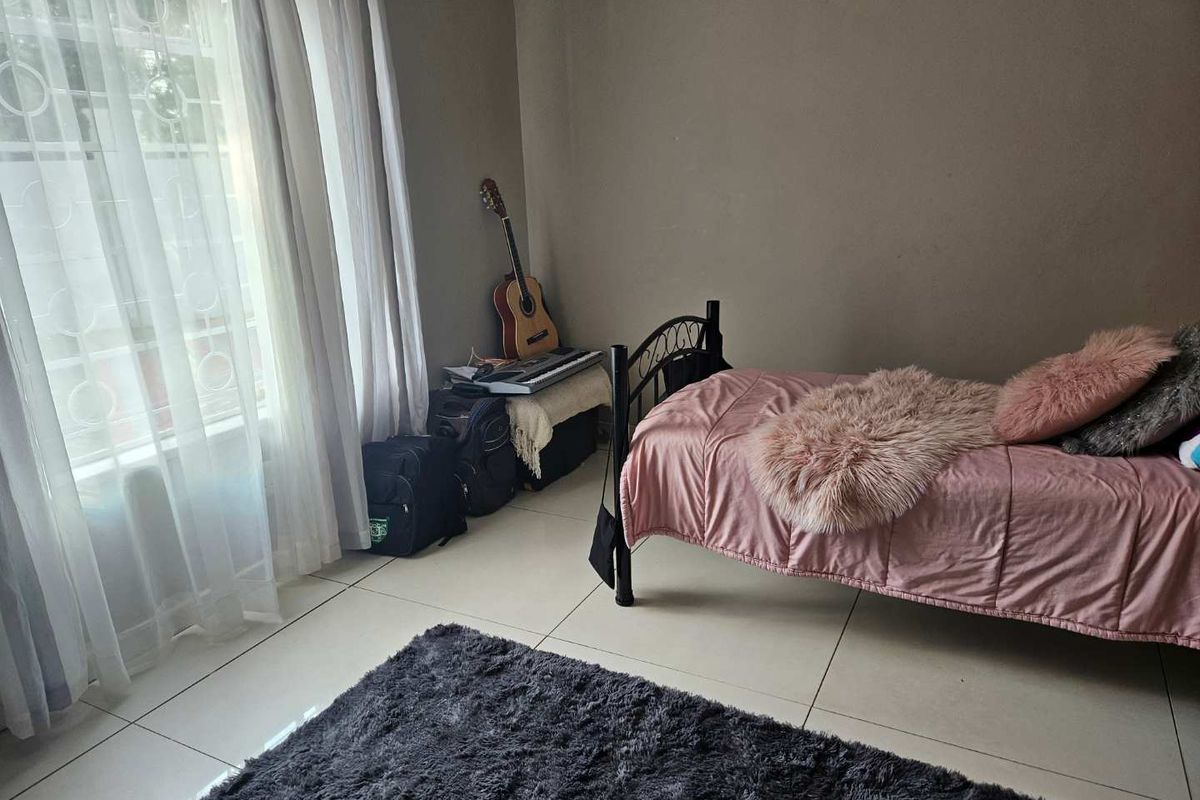 A bedroom featuring tiled flooring and a window with security bars, providing a functional and well-lit living space.