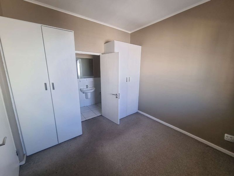 A clean, empty bedroom featuring neutral wall tones, carpeted flooring, and built-in cupboards, with direct access to an en-suite bathroom.