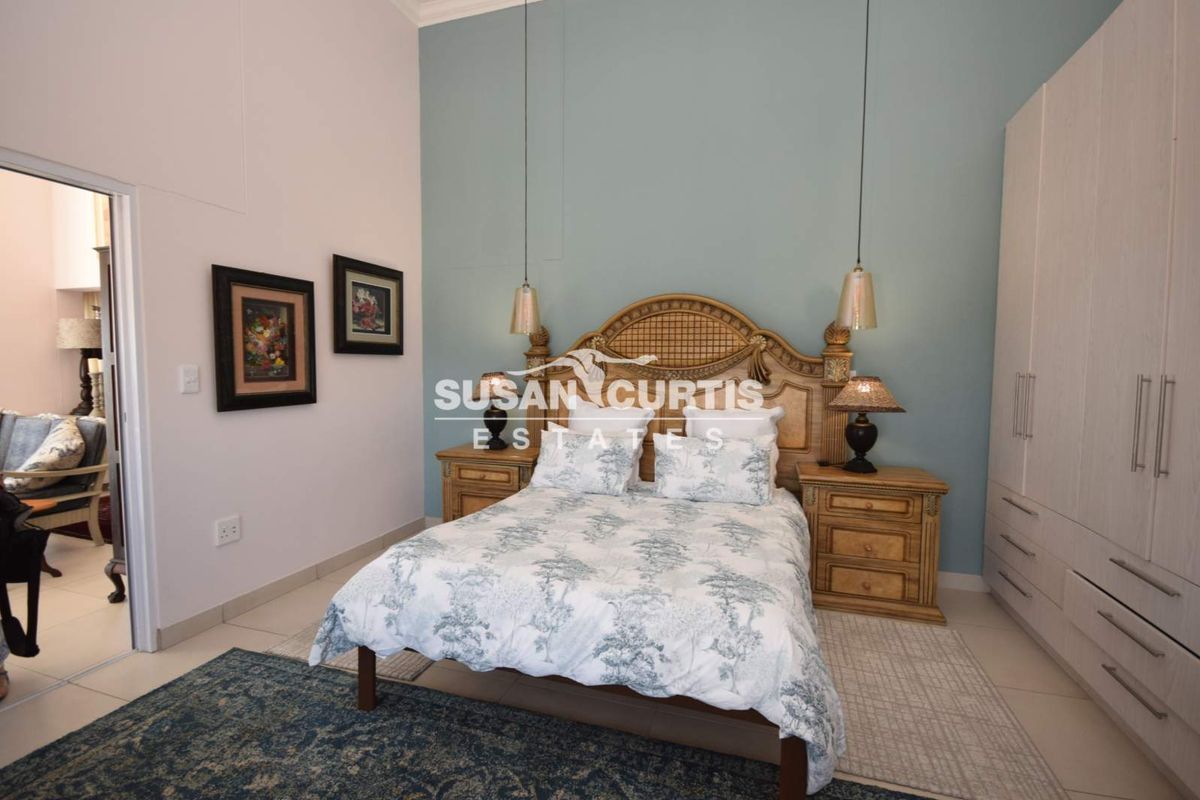 A well-maintained bedroom featuring a built-in wardrobe, high ceilings, and a feature wall with pendant lighting.