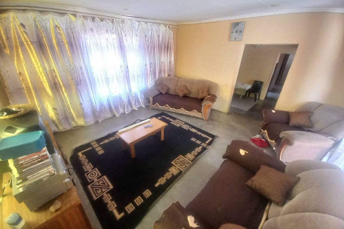 A living room featuring a large window with curtains, providing access to an adjacent room through an open doorway.
