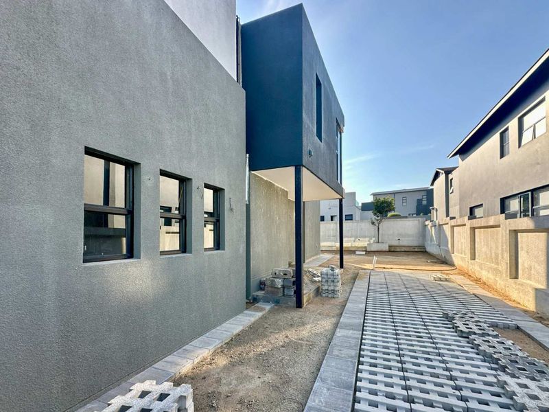 Rear exterior view of a modern house featuring a paved driveway, stucco facade, and unfinished landscaping area.