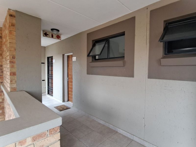 A clean, well-maintained apartment hallway featuring tiled flooring, brick accents, and secure access points with top-hung windows for ventilation.