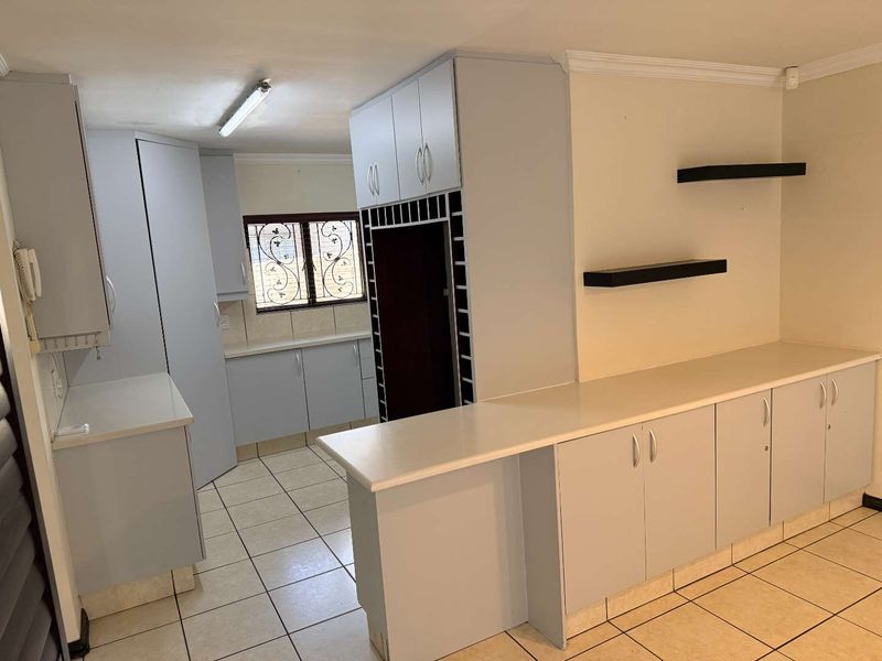 A functional kitchen featuring light grey built-in cabinetry, ample counter space, a built-in wine rack, and tiled flooring throughout.