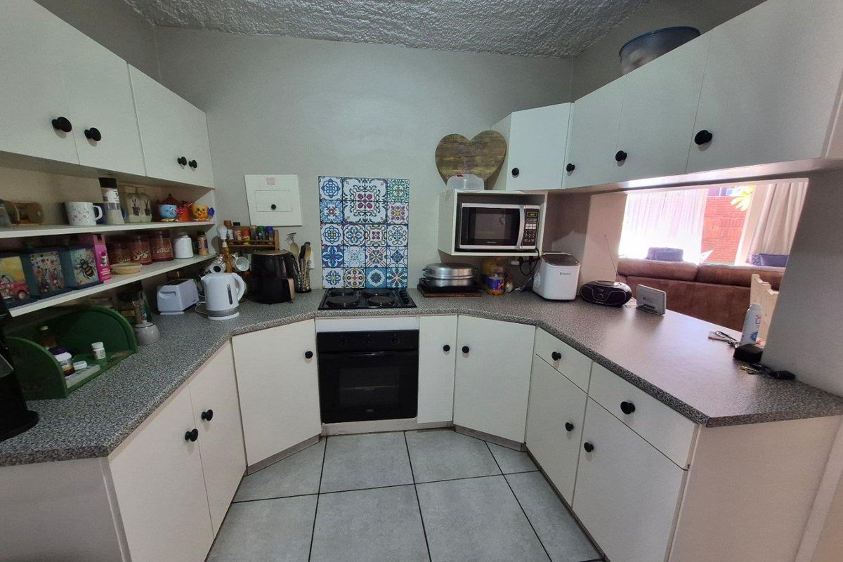 Compact kitchen featuring white cabinetry, built-in oven, gas hob, decorative tile splashback, and tiled flooring with a convenient serving hatch to the living area.