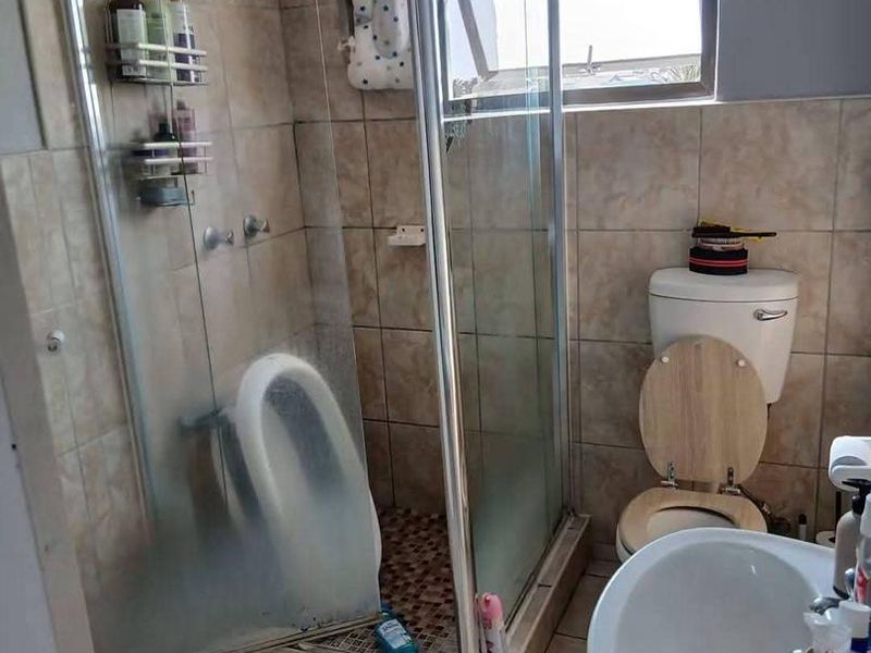 A functional bathroom featuring a corner shower enclosure, pedestal basin, and toilet with neutral ceramic tiling throughout.