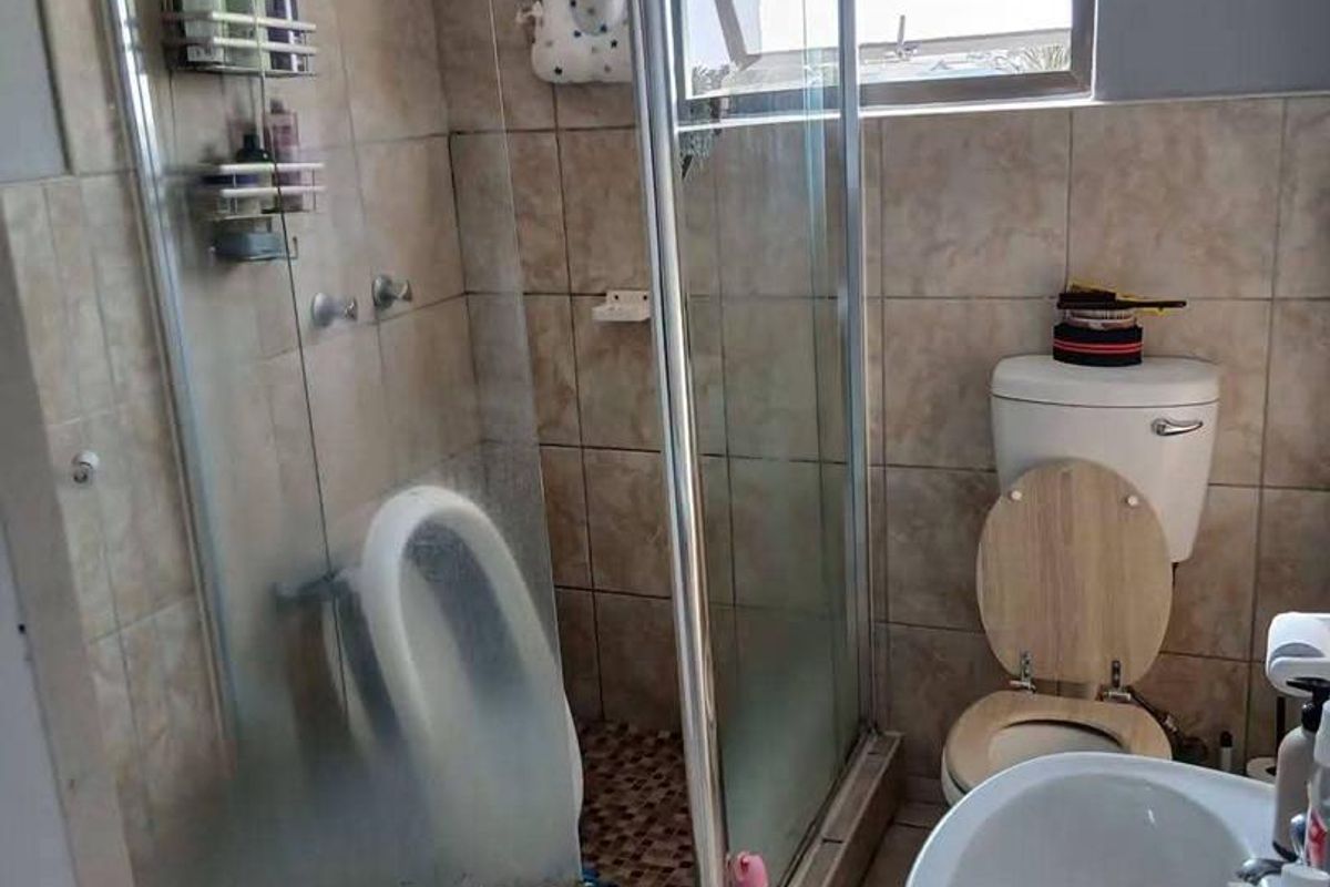 A functional bathroom featuring a corner shower enclosure, pedestal basin, and toilet with neutral ceramic tiling throughout.