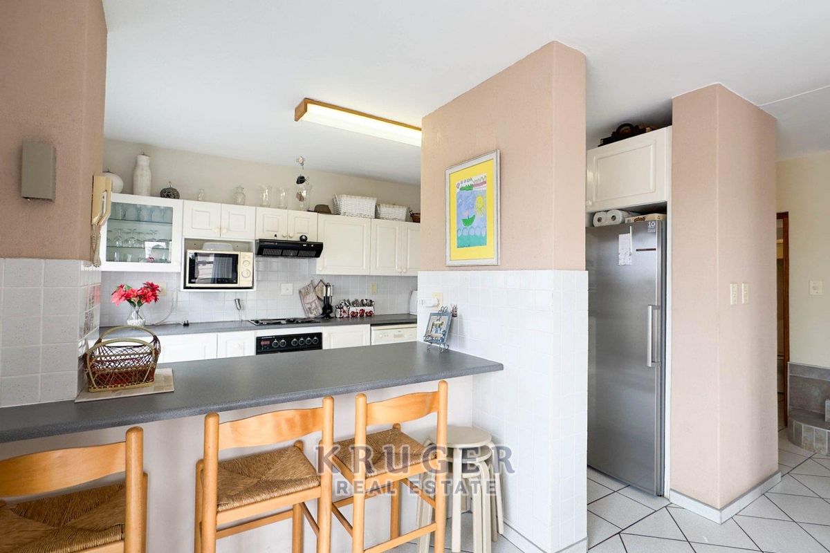 A functional kitchen featuring white cabinetry, a breakfast bar with a dark countertop, built-in oven, hob, and extractor fan, adjacent to a staircase.