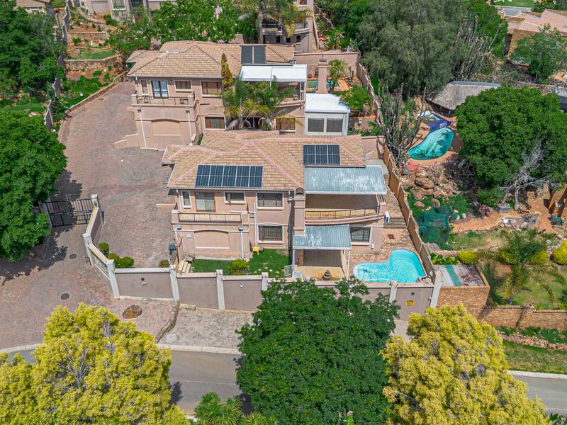 Aerial view of a multi-level residential property featuring a swimming pool, solar panels, paved driveway, and established garden areas.