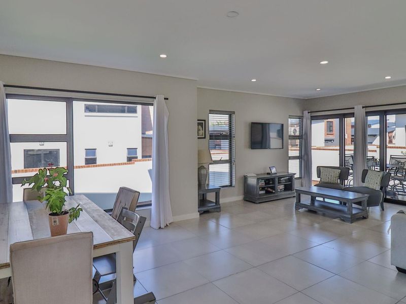Spacious open-plan living and dining area featuring modern tiled flooring, recessed lighting, and large aluminium sliding doors leading to an outdoor patio.