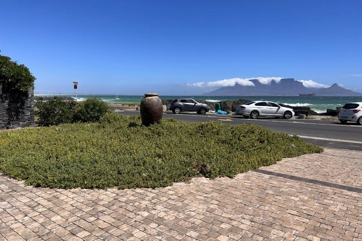 A scenic coastal view overlooking the ocean and Table Mountain from a paved walkway with landscaped garden features.