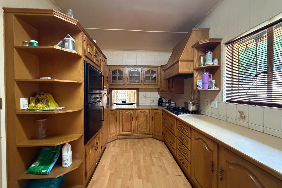 A functional kitchen featuring extensive built-in wooden cabinetry, a gas hob, integrated oven, and tiled backsplash, offering a traditional layout with ample storage space.