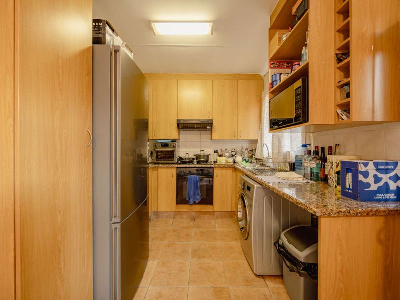 A functional galley-style kitchen featuring light wood cabinetry, granite countertops, integrated appliances, and tiled flooring, offering efficient workspace and storage.
