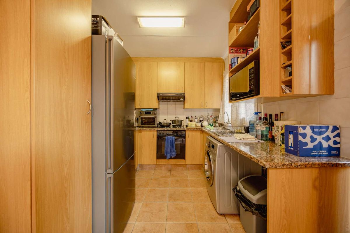 A functional galley-style kitchen featuring light wood cabinetry, granite countertops, integrated appliances, and tiled flooring, offering efficient workspace and storage.