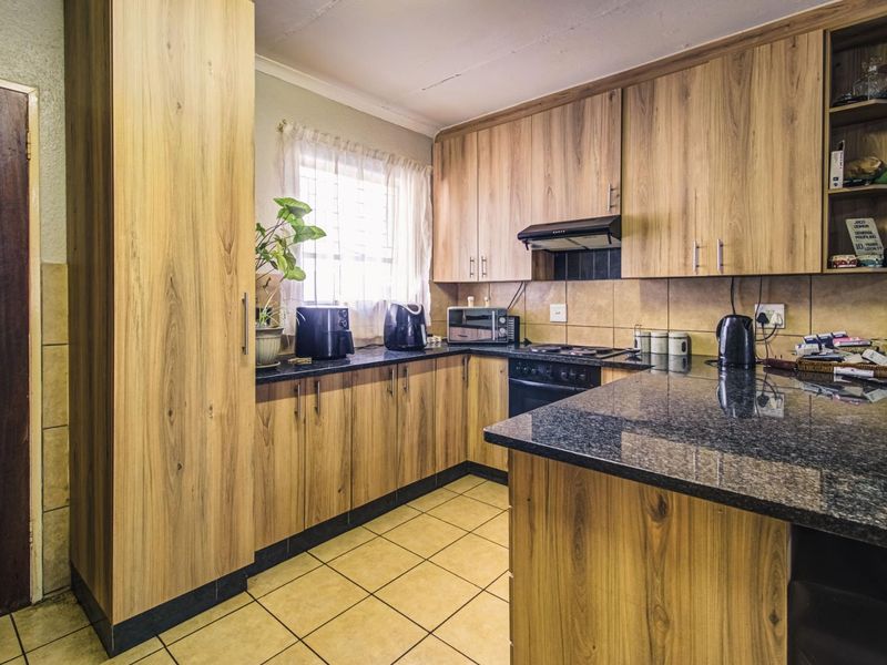 Functional kitchen featuring wood-look cabinetry, granite countertops, built-in oven, hob, and extractor fan with tiled flooring and backsplash.