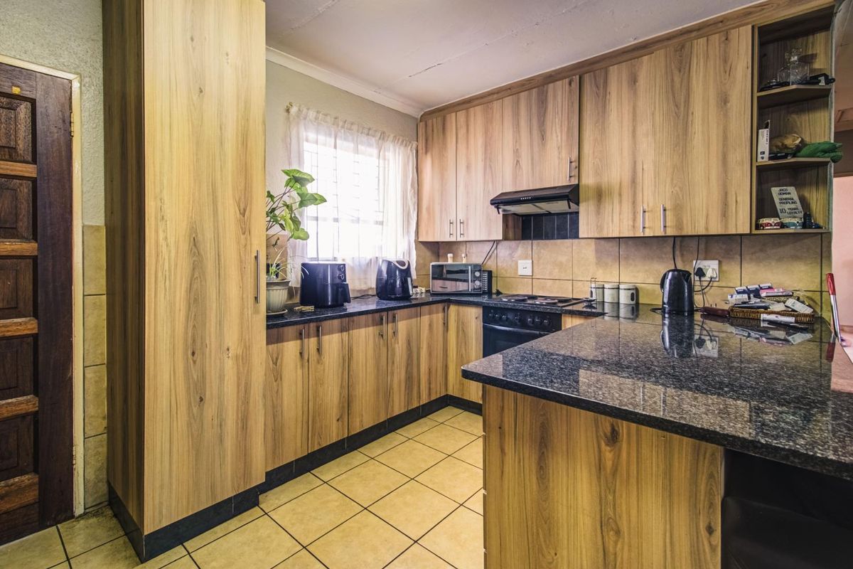 Functional kitchen featuring wood-look cabinetry, granite countertops, built-in oven, hob, and extractor fan with tiled flooring and backsplash.