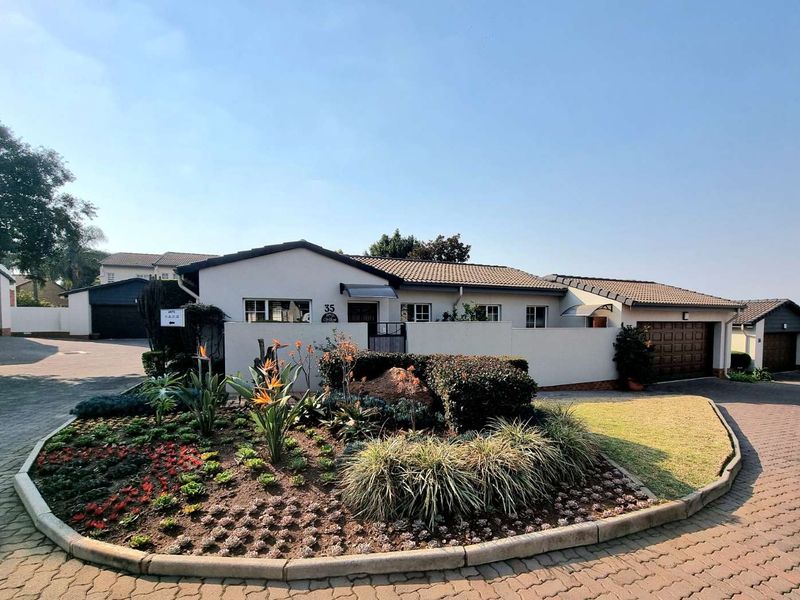 Front elevation of a townhouse featuring a well-maintained landscaped garden, paved driveway, and integrated garage.
