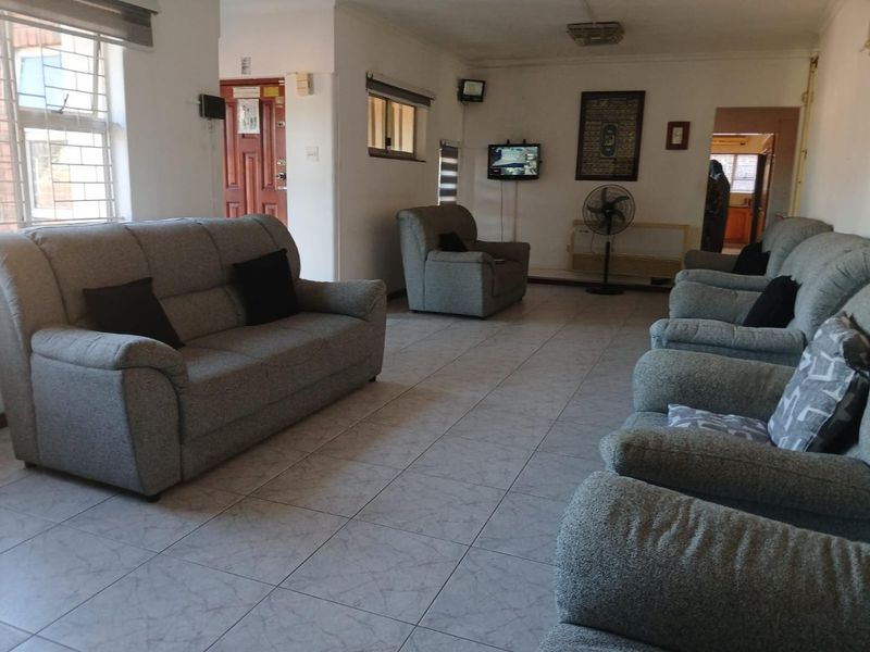 A spacious living room featuring tiled flooring, neutral walls, and security bars on the windows, providing a functional and well-lit living area.