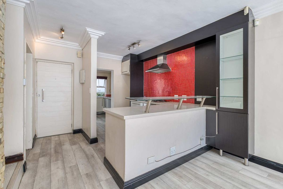 A modern kitchen featuring a breakfast bar, striking red mosaic backsplash, built-in dark cabinetry with glass shelving, and light-toned laminate flooring.