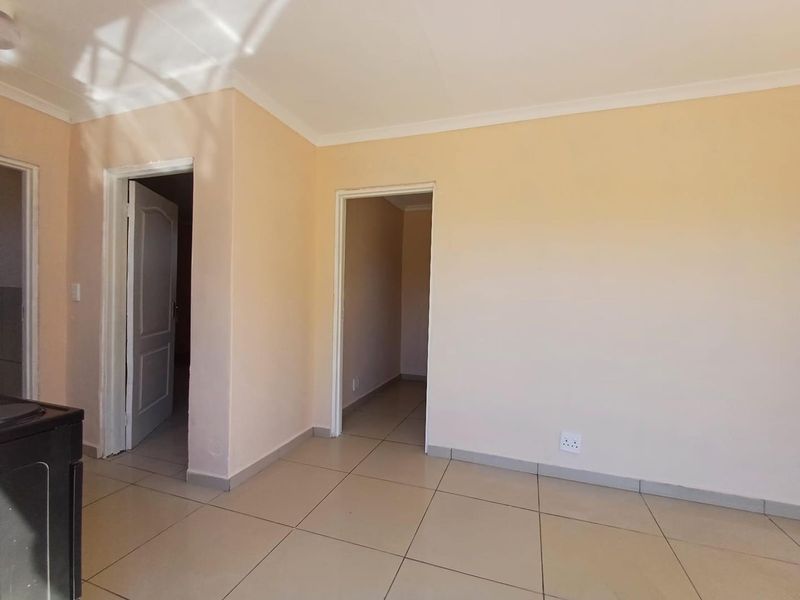A bright, empty living area featuring neutral tiled flooring, coved ceilings, and access to adjacent rooms through standard doorways.