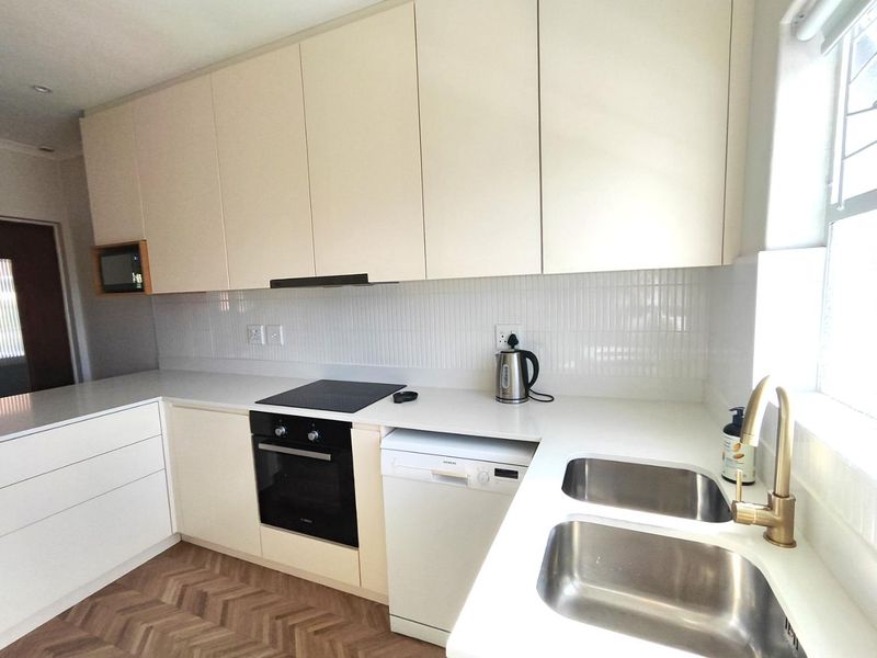 Modern kitchen featuring sleek cream cabinetry, stone countertops, a double sink with brass fixtures, built-in appliances, and stylish herringbone flooring.