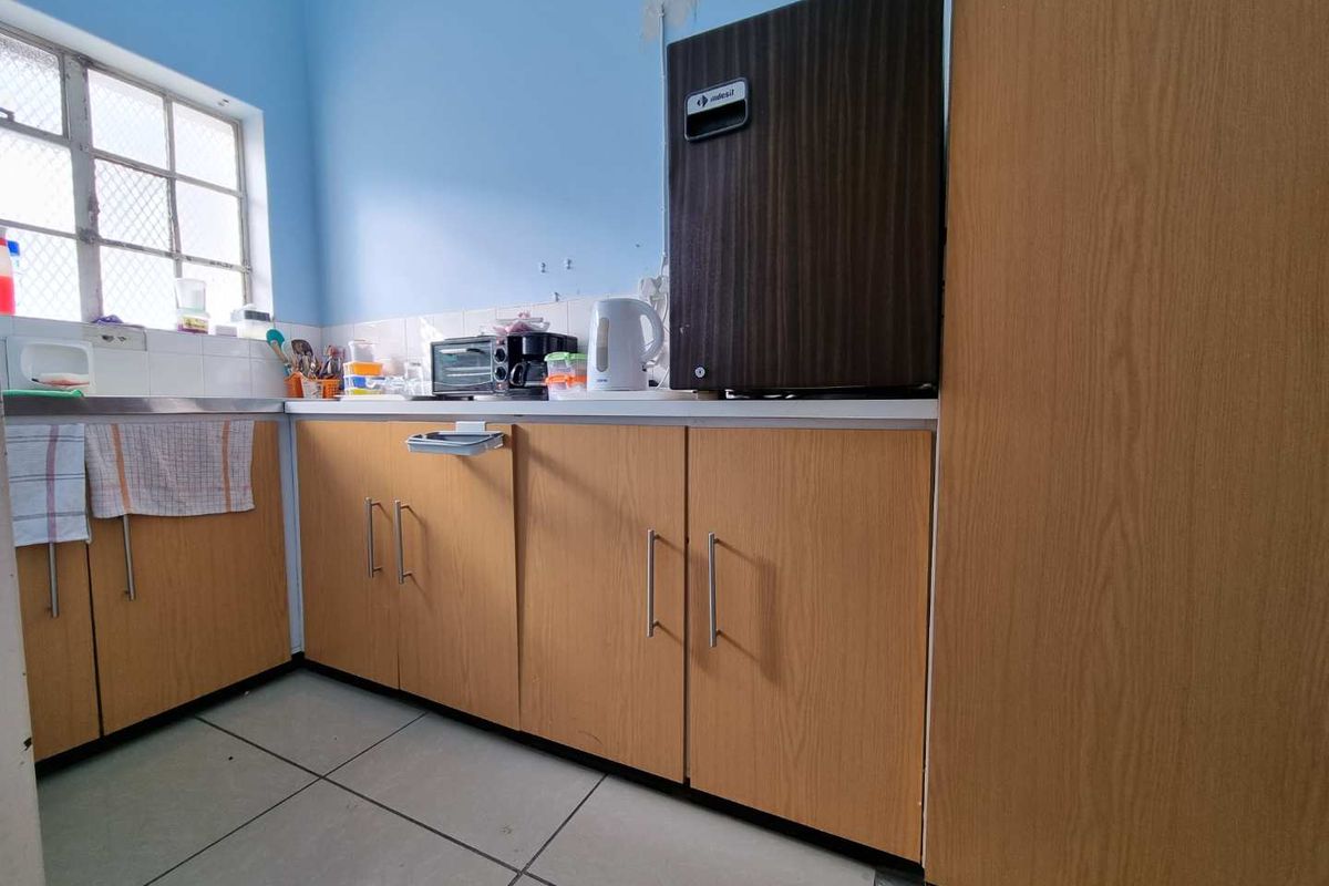 A compact kitchen area featuring light wood-finish cabinetry, tiled flooring, and a window, requiring some cosmetic updates to the wall surfaces.