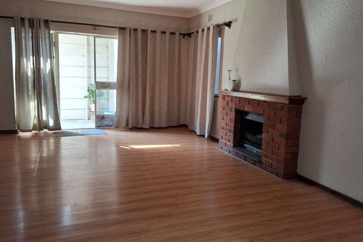 Spacious living room featuring laminate flooring and a classic brick fireplace, with direct access to an outdoor patio area through sliding glass doors.