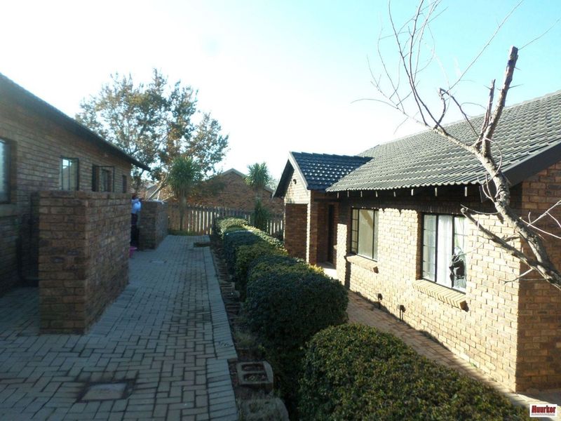 Exterior view of the apartment complex featuring face brick construction, a tiled roof, and a paved walkway bordered by established hedges.