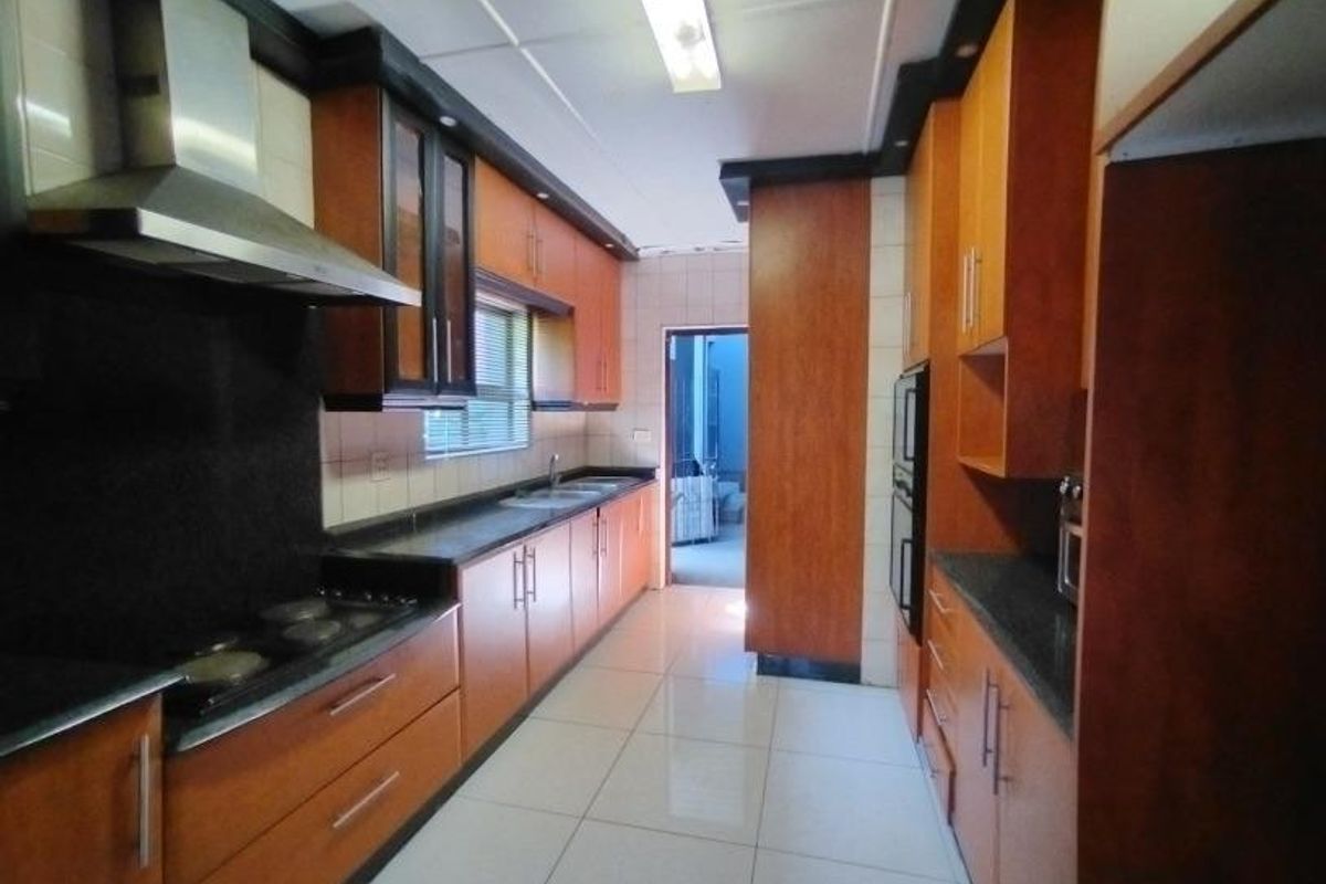 A functional galley-style kitchen featuring wood-finish cabinetry, dark countertops, integrated appliances, and tiled flooring, offering a clean and practical workspace.