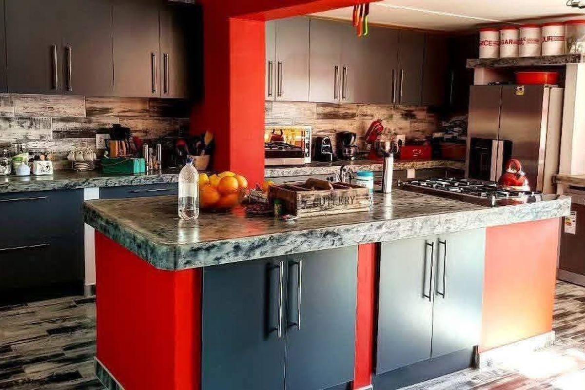 Modern kitchen featuring dark cabinetry, a central island with stone-look countertop, integrated gas hob, and contrasting red accent walls.
