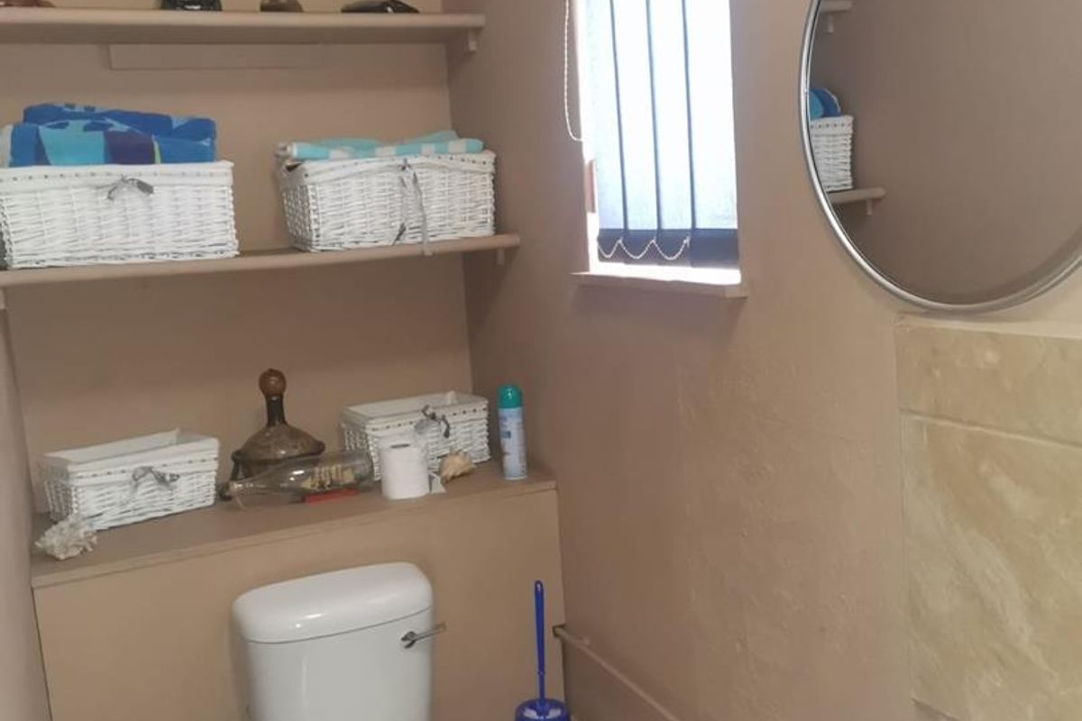 A functional bathroom featuring a standard toilet, pedestal basin, and built-in shelving for storage, finished with neutral wall tones.