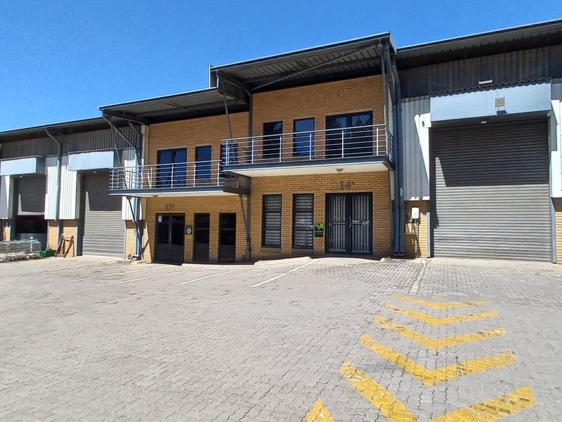 Front elevation of an industrial warehouse complex featuring roller shutter doors, brick facade, and upper-level balcony access.