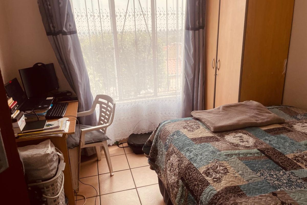 A functional bedroom featuring tiled flooring, a built-in wardrobe, and a large window providing natural light.