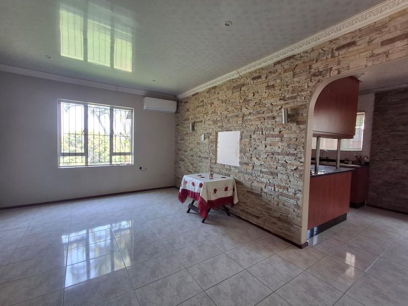 Open-plan living area featuring a stone-clad feature wall, tiled flooring, and a split-system air conditioner, with an arched transition to the kitchen area.