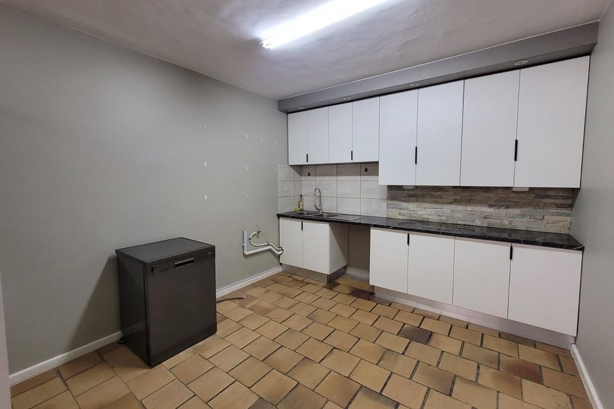 A functional kitchen area featuring white cabinetry, dark countertops, a tiled backsplash, and durable floor tiles, providing a clean and practical workspace.