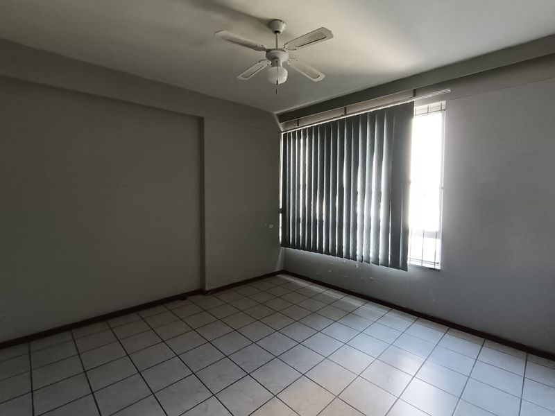 An empty bedroom featuring tiled flooring, a ceiling fan, and vertical blinds, requiring minor cosmetic updates to the wall finishes.