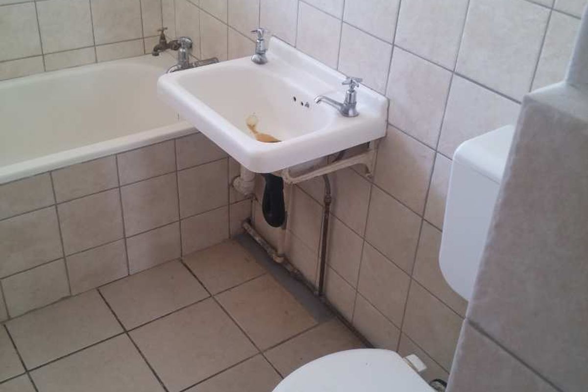 A functional bathroom featuring a bathtub, wall-mounted basin, and toilet with neutral ceramic tiling throughout.