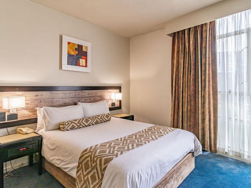 A bedroom featuring a built-in headboard with integrated lighting and large windows with floor-to-ceiling curtains.