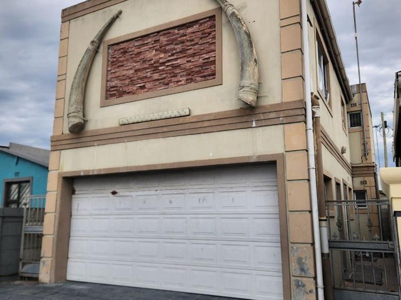 Front elevation of a multi-story property featuring a sectional garage door, stone cladding accents, and decorative exterior elements with paved driveway access.