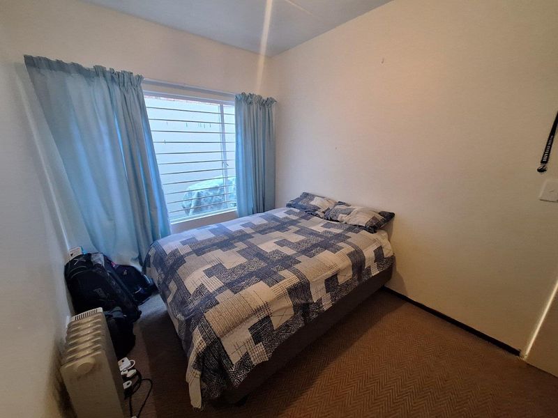 A standard bedroom featuring carpeted flooring and a window fitted with security bars.