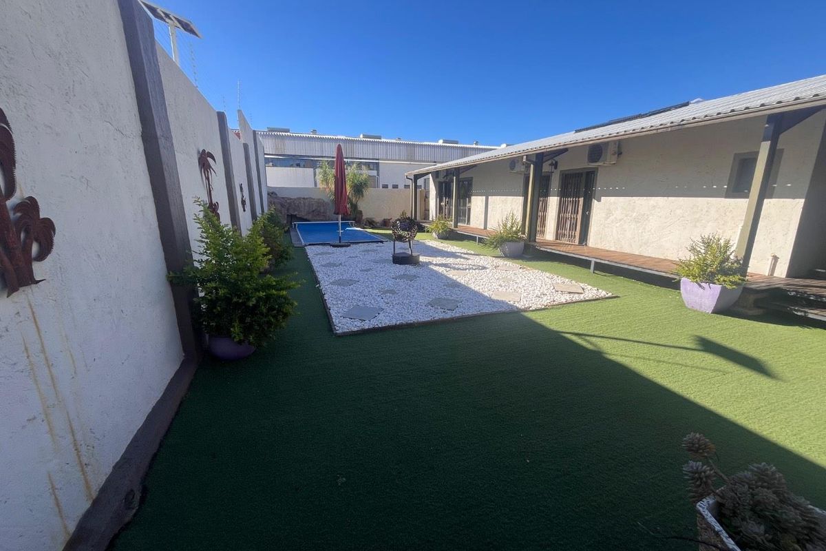 Outdoor courtyard area featuring artificial turf, a gravel garden bed, a small plunge pool, and a covered wooden deck walkway.