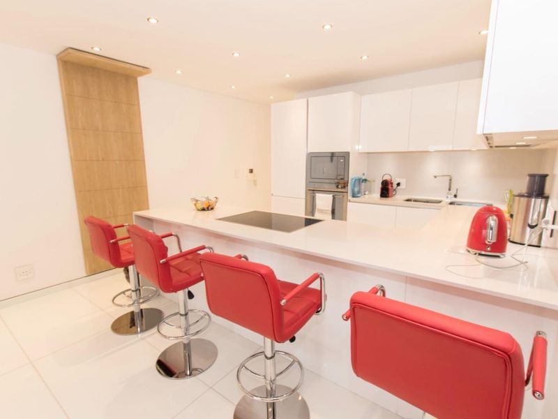 Modern kitchen featuring white cabinetry, stone countertops, integrated appliances, and a breakfast bar with recessed lighting.