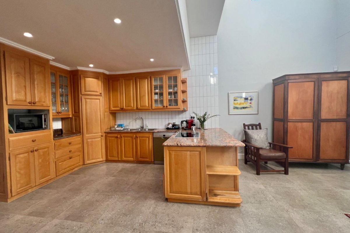 Spacious kitchen featuring timber cabinetry, granite countertops, a central island with a built-in cooktop, and high ceilings with a skylight.