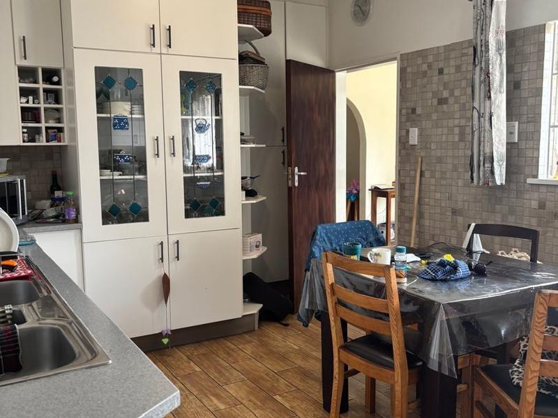 A functional kitchen featuring white built-in cabinetry, glass-fronted display units, a double sink, and tiled backsplash with wood-look floor tiles.