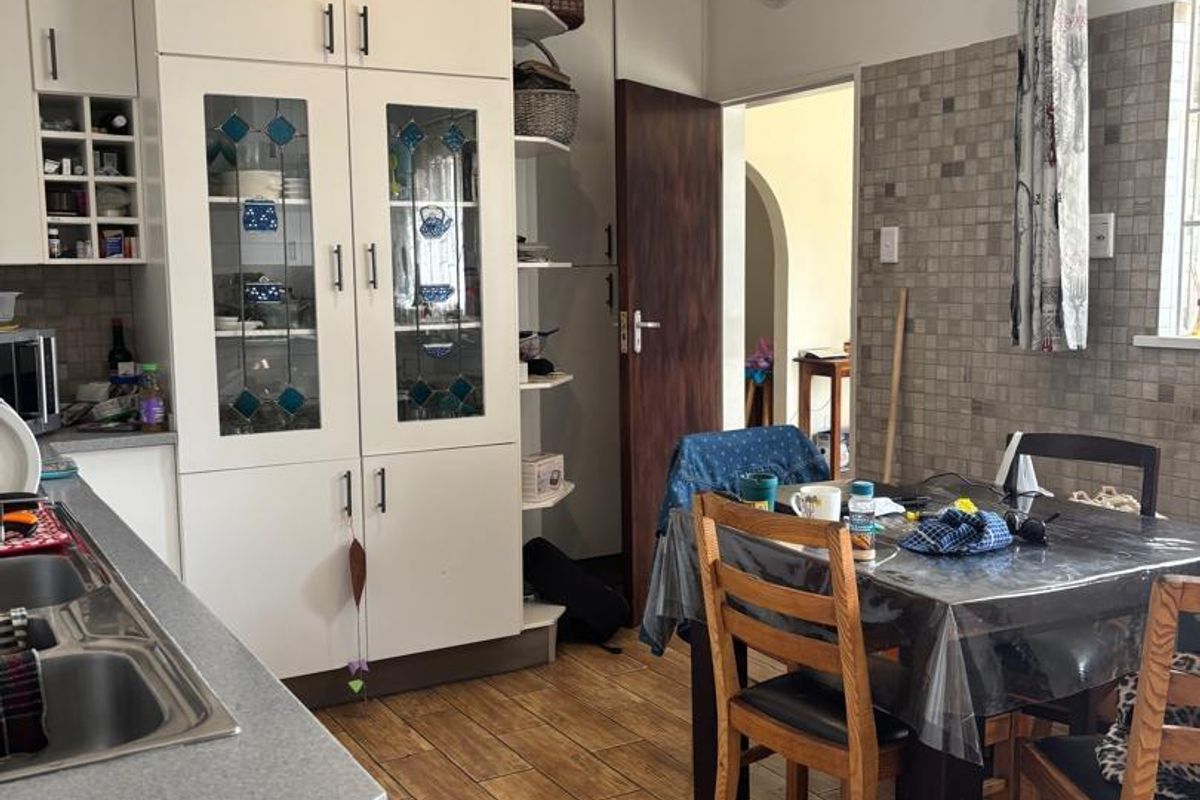 A functional kitchen featuring white built-in cabinetry, glass-fronted display units, a double sink, and tiled backsplash with wood-look floor tiles.