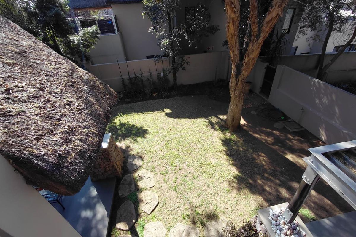 An elevated view of a private rear garden featuring a thatched roof section, stone stepping stones, and established trees within a walled boundary.
