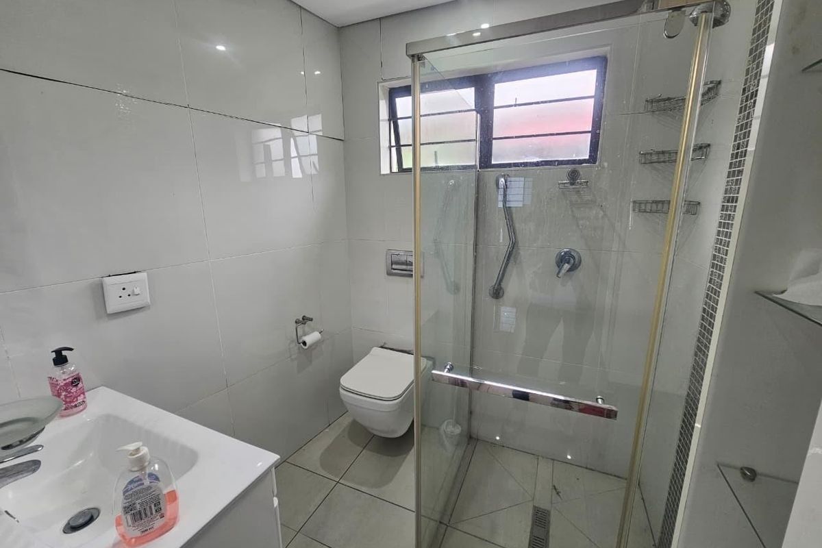 A modern bathroom featuring a glass shower enclosure, wall-mounted toilet, and a vanity basin with neutral tiled finishes throughout.