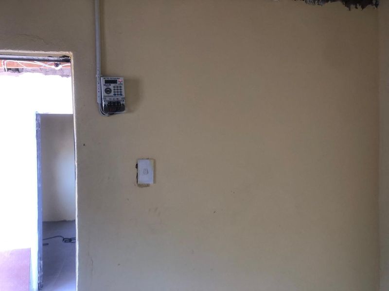 Interior view showing a wall with a prepaid electricity meter, light switch, and visible unfinished ceiling and wall edges.