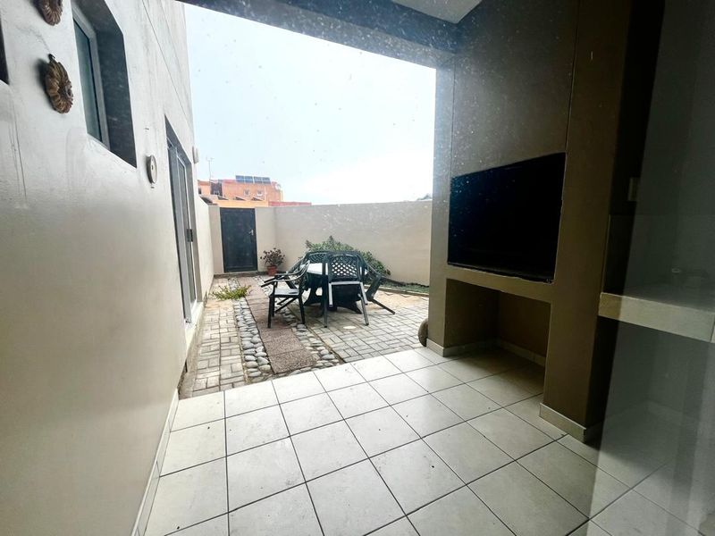 Covered patio area featuring a built-in braai, tiled flooring, and access to a private paved courtyard space.