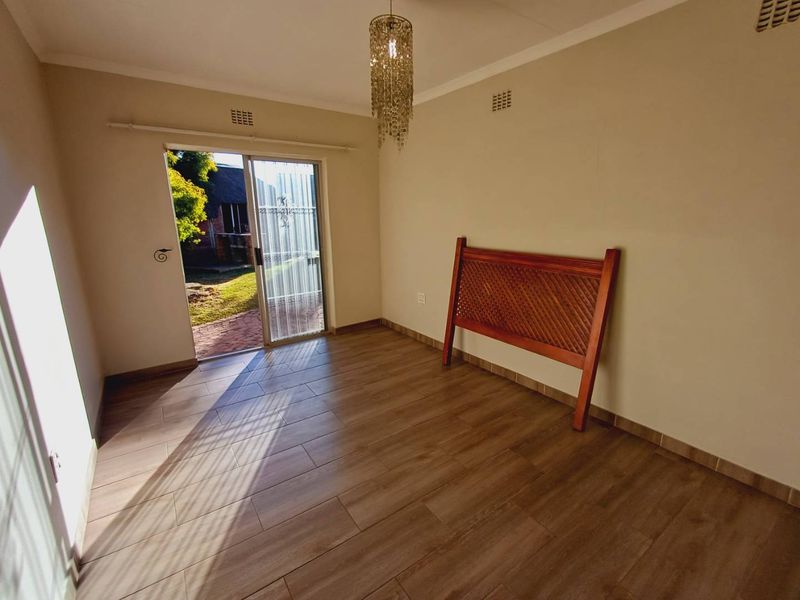 A bright, empty bedroom featuring modern wood-look floor tiles and a sliding glass door providing direct access to the garden.