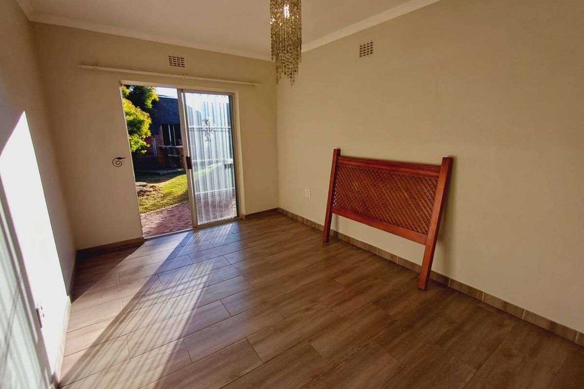 A bright, empty bedroom featuring modern wood-look floor tiles and a sliding glass door providing direct access to the garden.